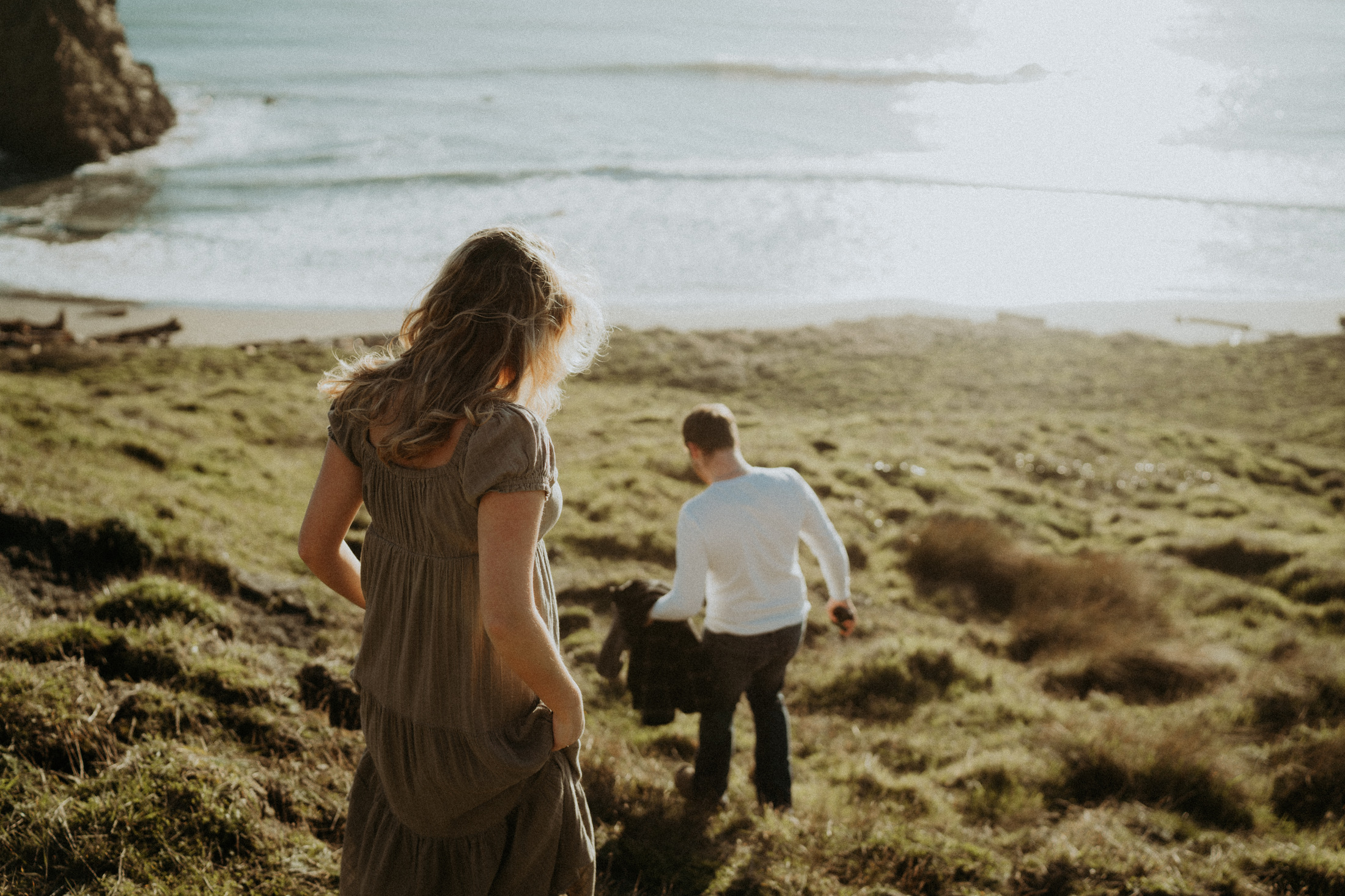 Gabe and Alena walking toward an Oregon beach from a coastal hillside