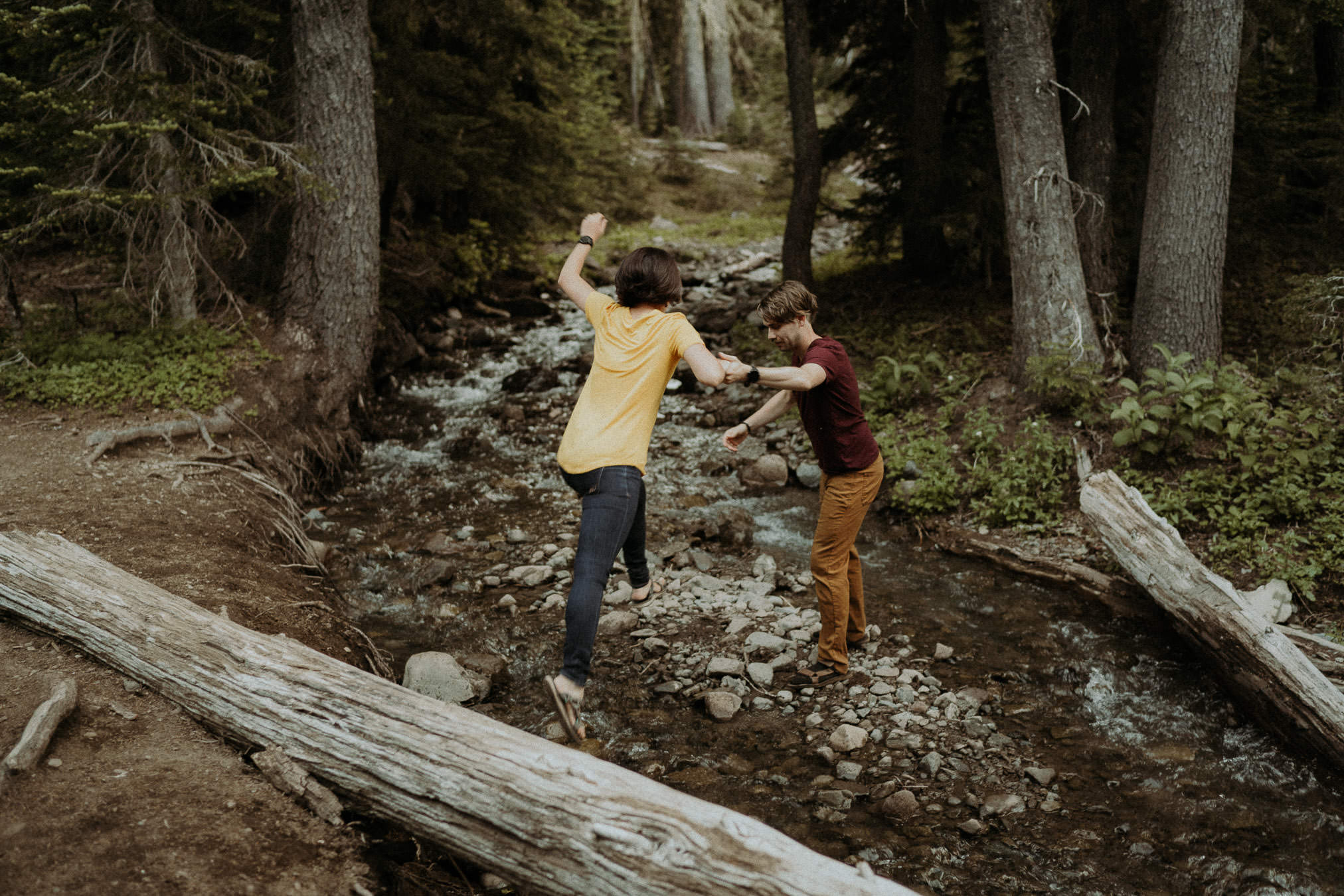 Larry and Alison holding hands as they cross a fallen tree in the forest