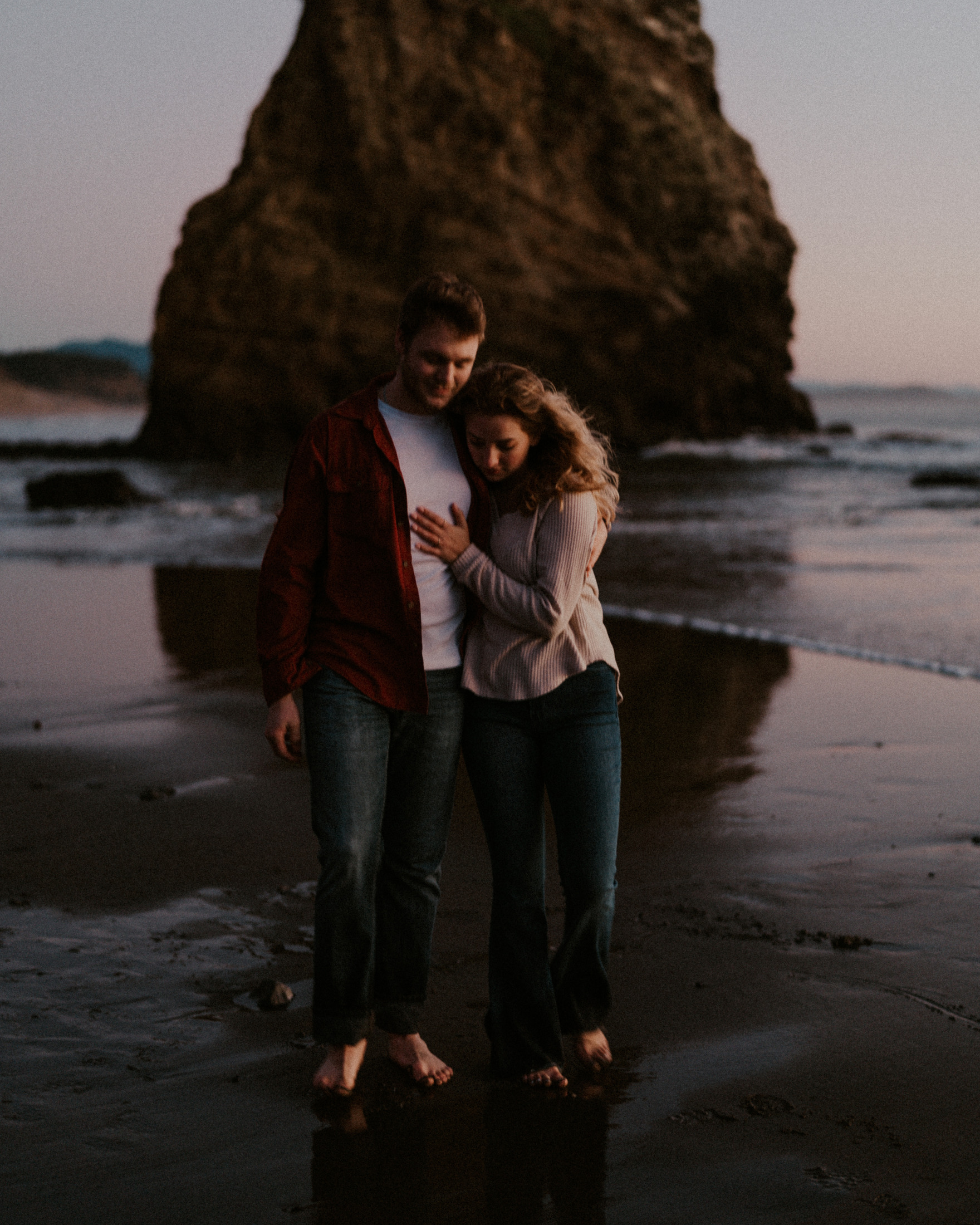 Gabe and Alena embracing beside a sea stack as the light fades