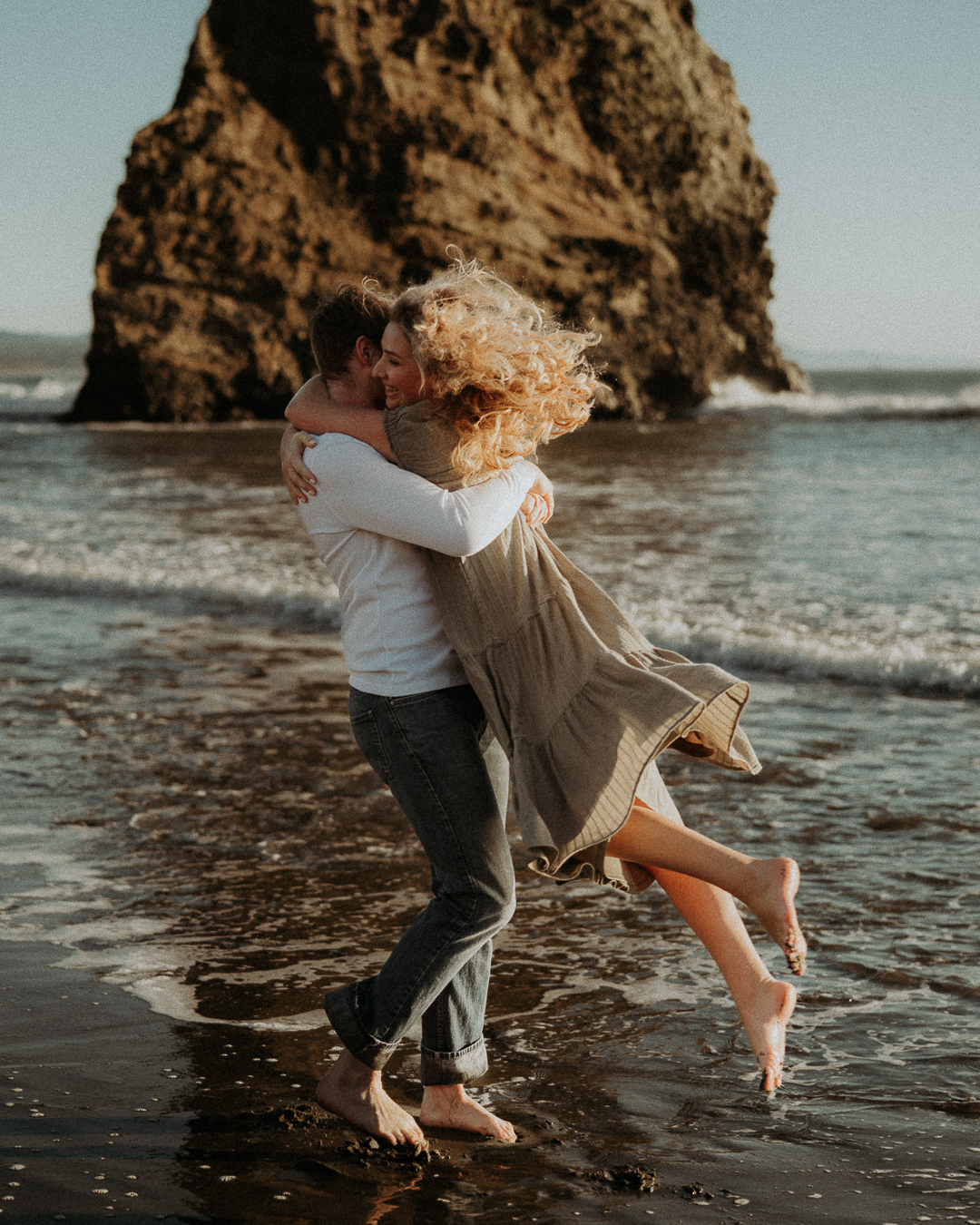 Gabe lifting Alena beside a sea stack at the edge of the ocean