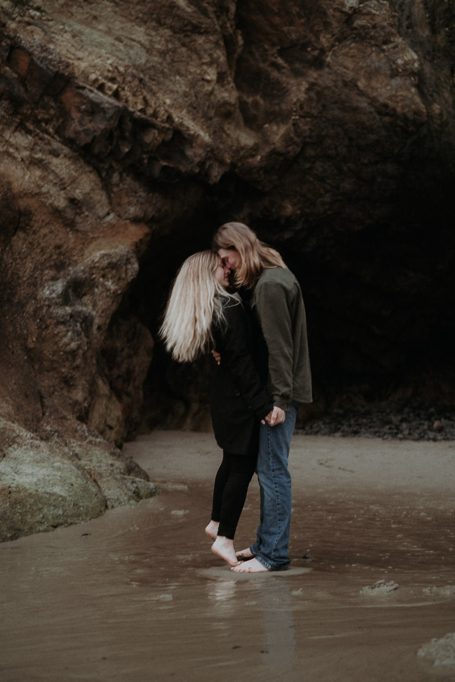 Hannah and Clay embracing in shallow water beside a coastal rock formation