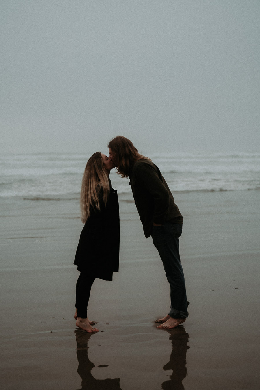Hannah and Clay leaning toward a kiss with their reflections in wet sand