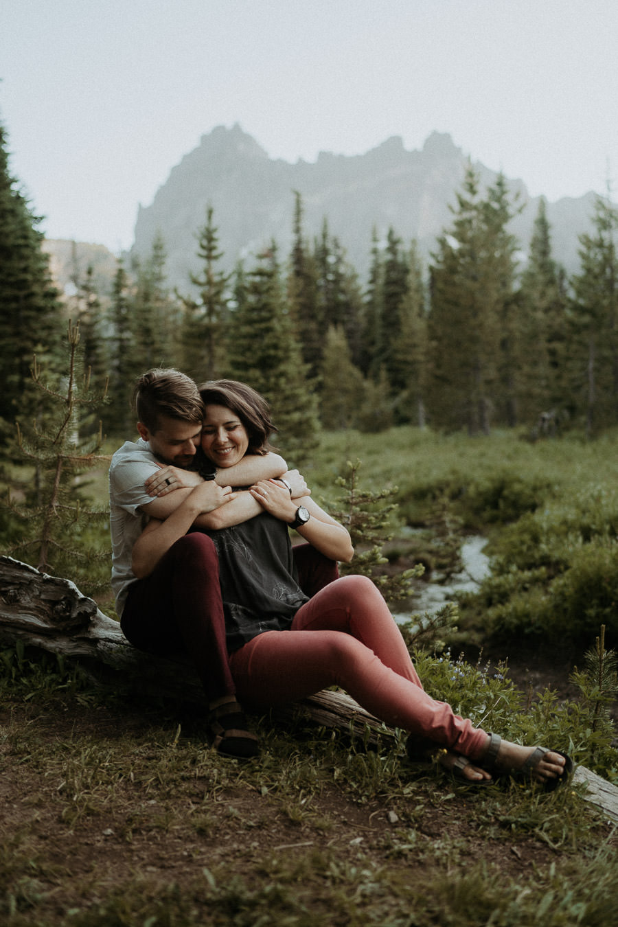 Larry and Alison sitting together beneath the mountains and evergreen trees