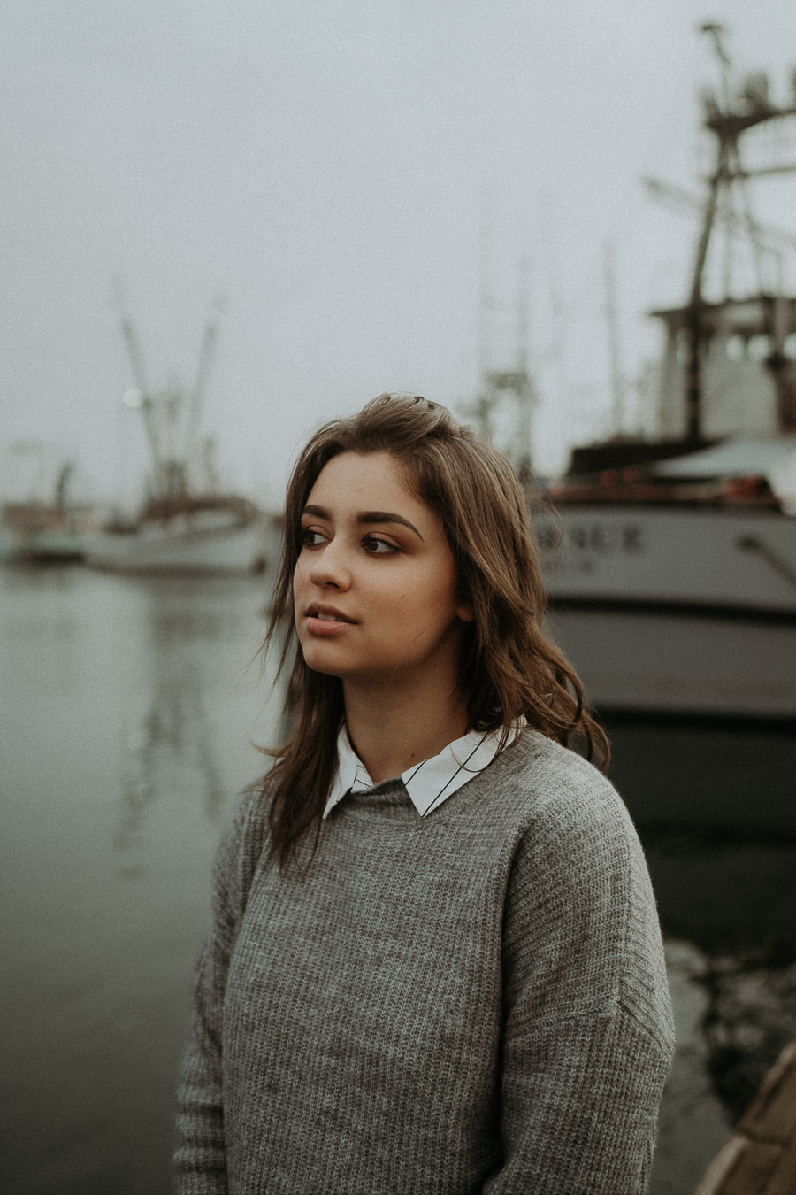 A woman in a gray sweater photographed beside fishing boats
