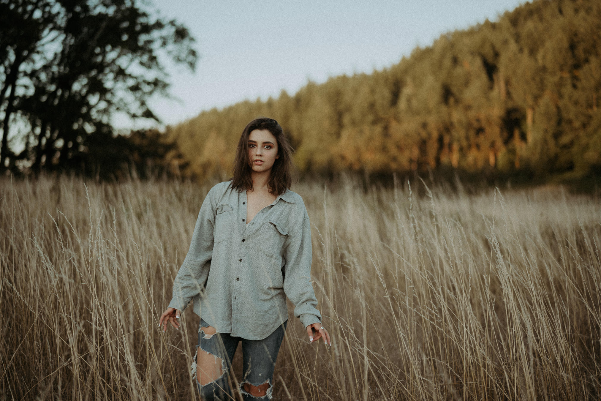 A woman in a denim jacket standing in a meadow beside trees
