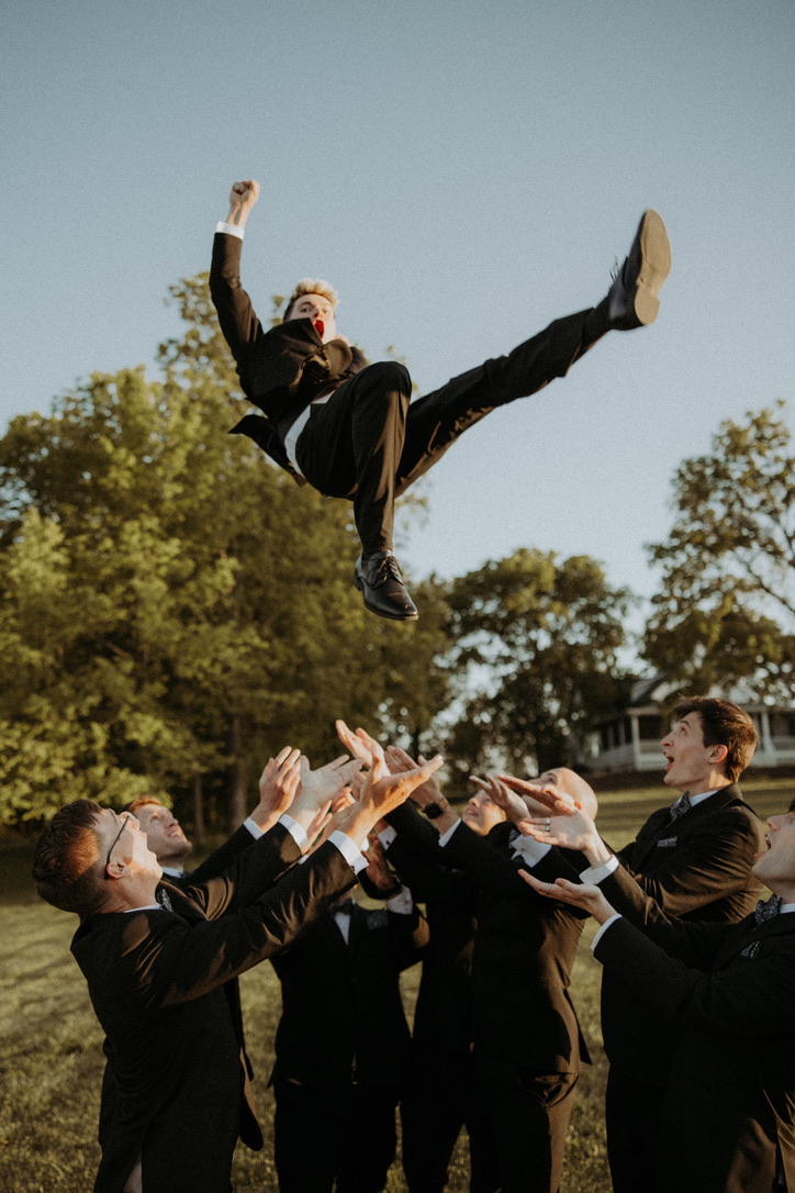 Groomsmen tossing a friend into the air outside at a wedding