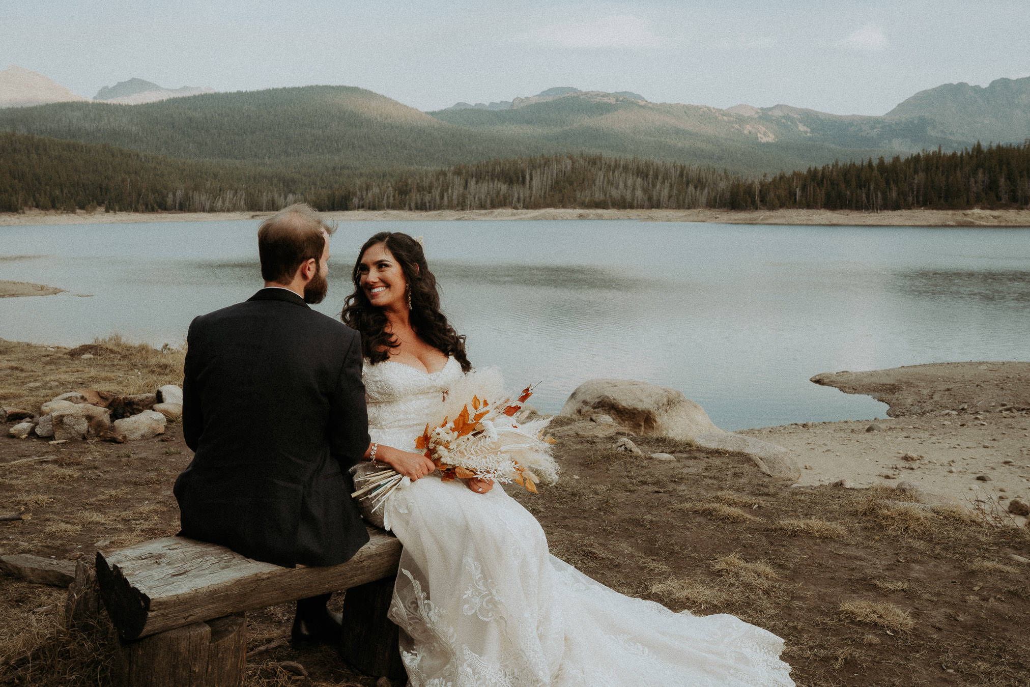 Sam and Savanna sitting together beside a lake with Colorado mountains behind them